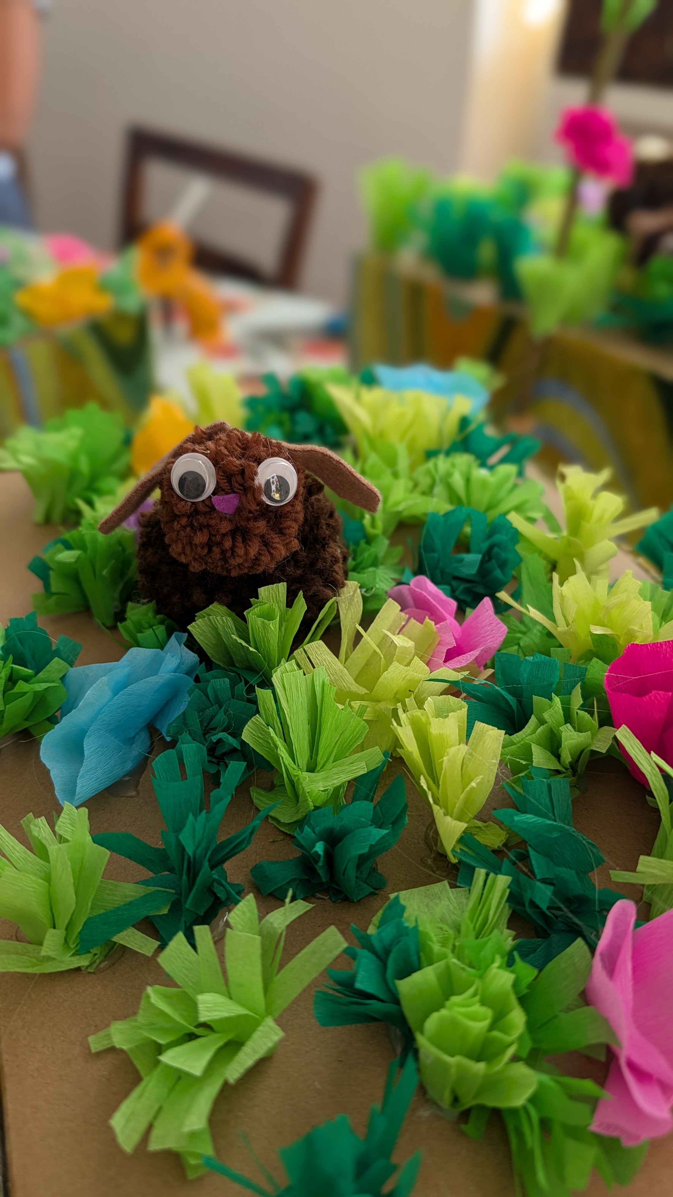 Selbstgebastelter Bommelhase zwischen bunten Krepppapier-Blumen