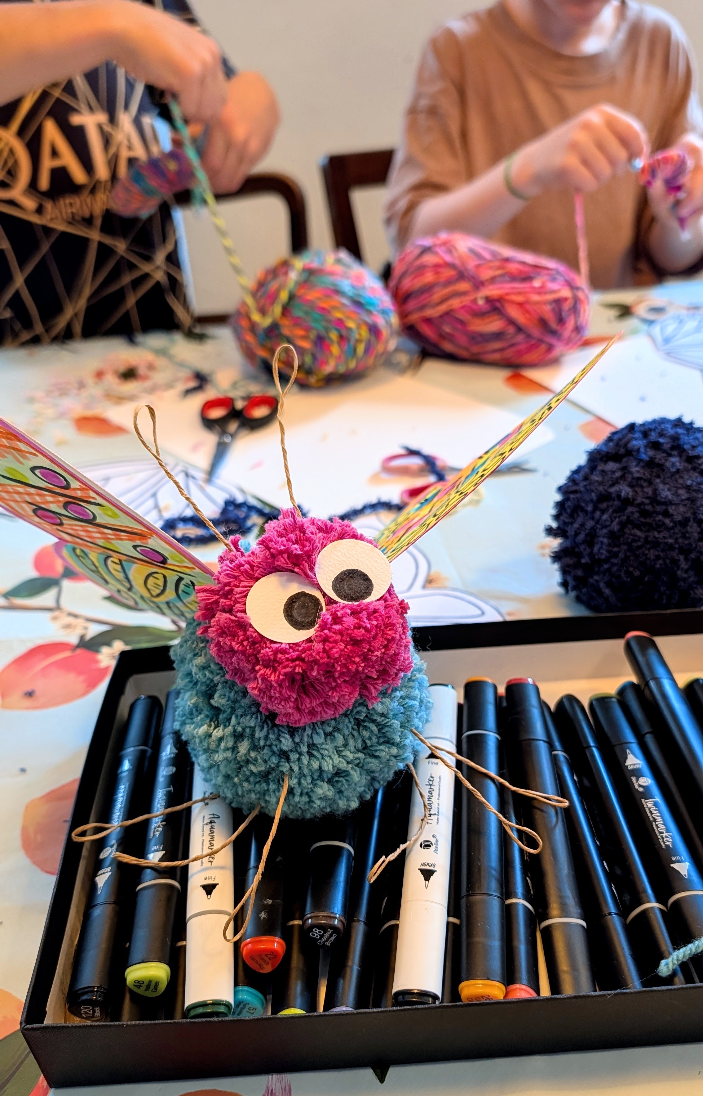 Selbstgebastelter Pompon-Schmetterling mit Wackelaugen und bemalten Flügeln