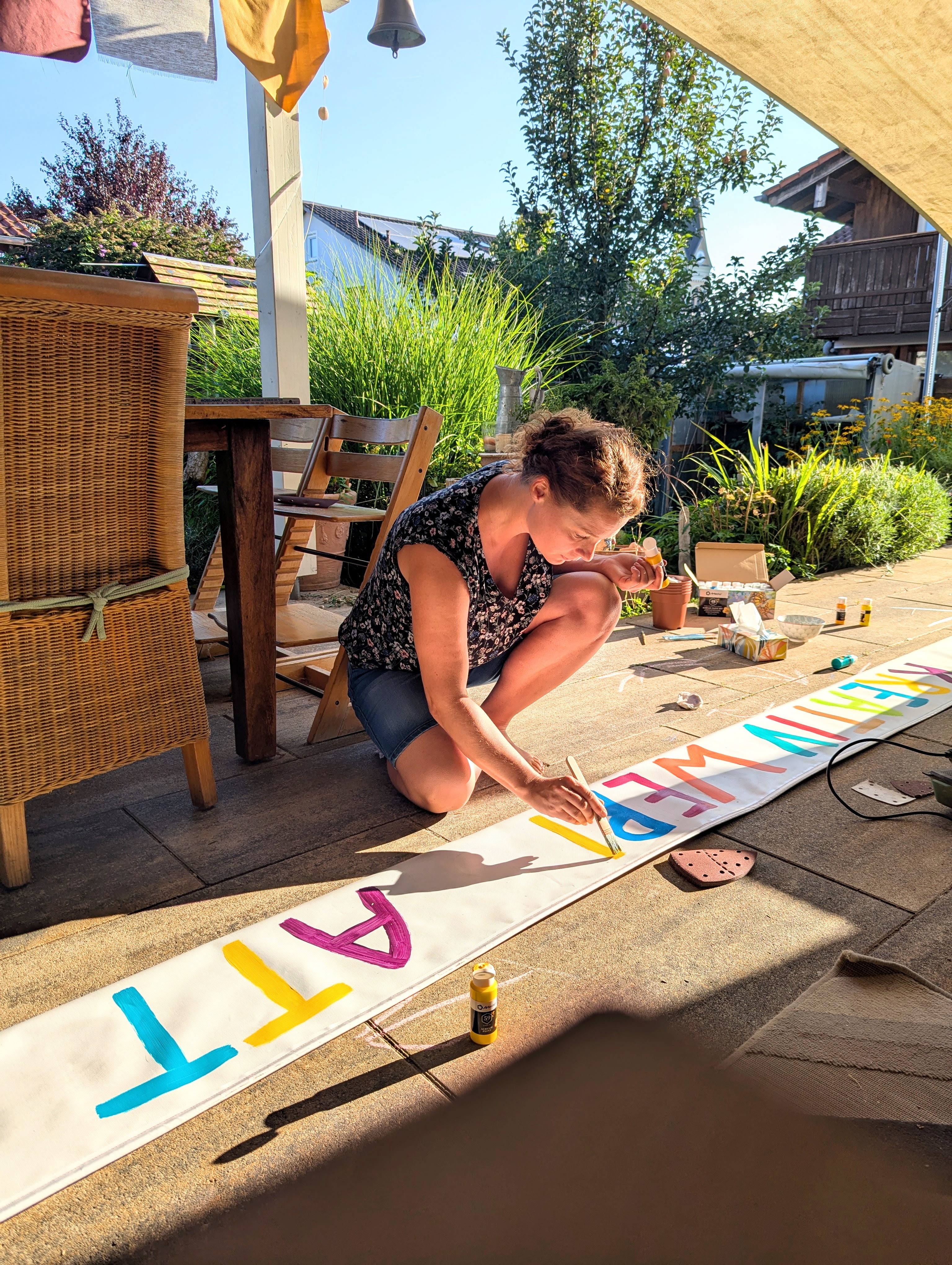 Uli bemalt kniend ein buntes Banner im Garten