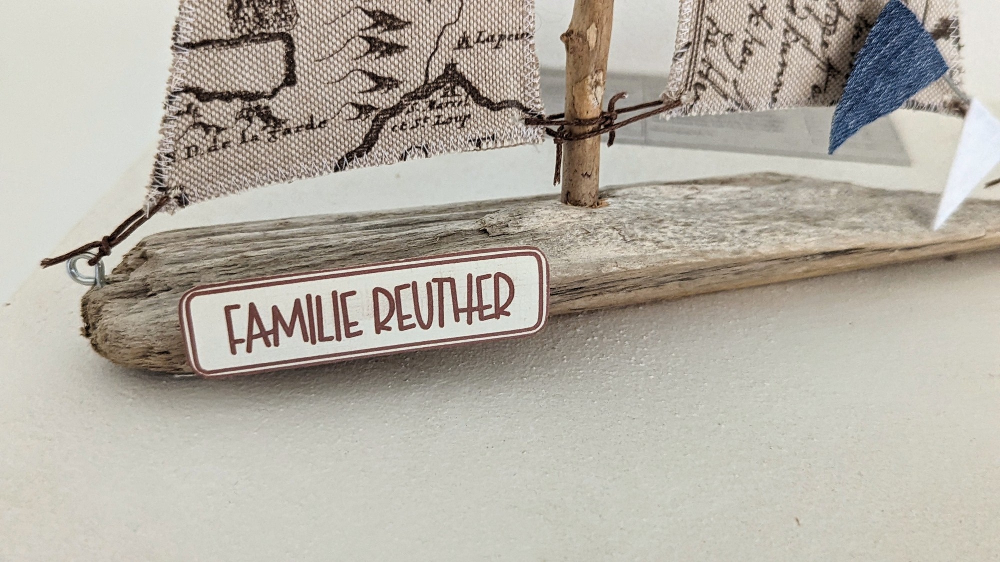 Detailaufnahme des Namensschilds „Familie Reuther“ auf einem Treibholzboot