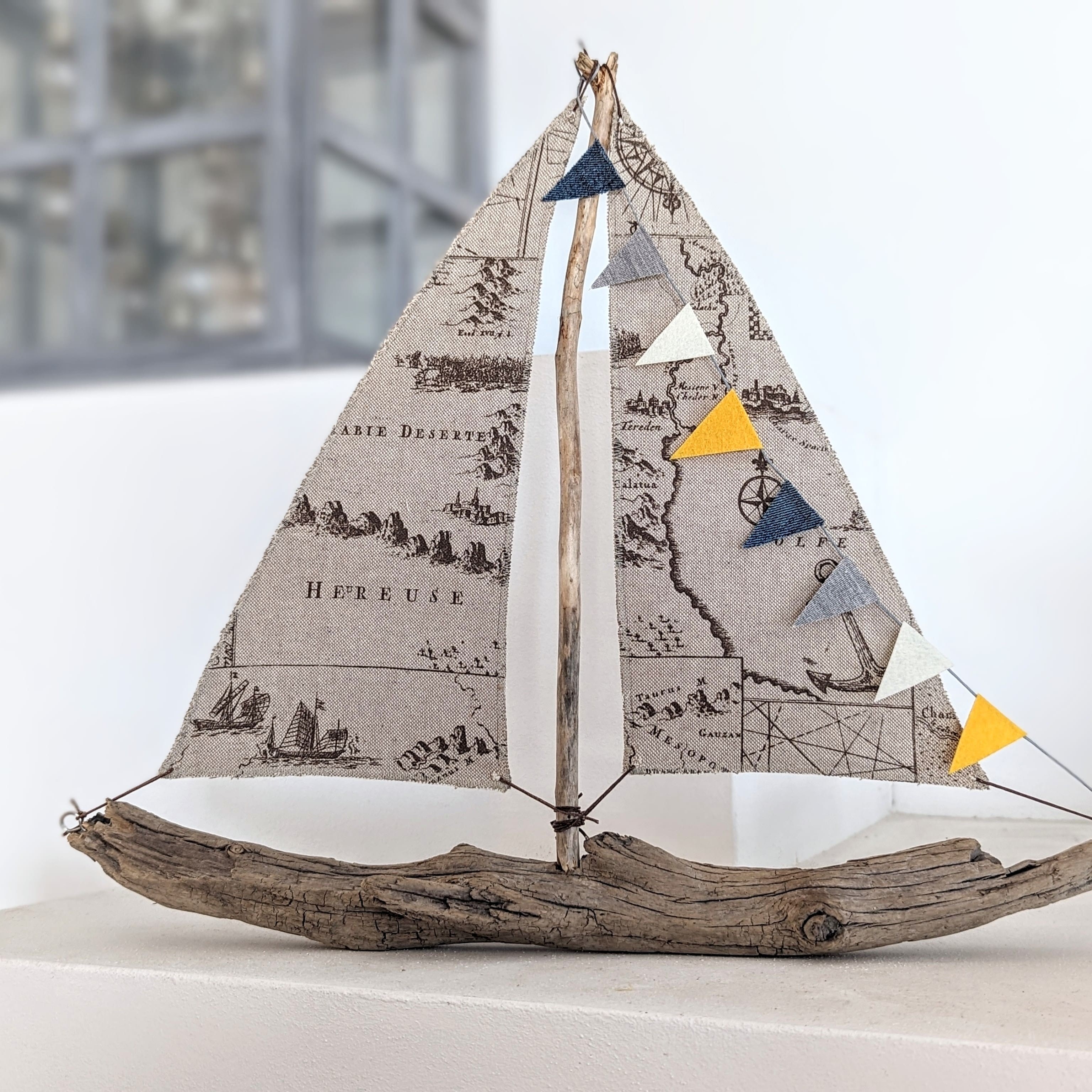 Großes Treibholzboot mit Seekarten-Segel und gelb-blauer Wimpelkette