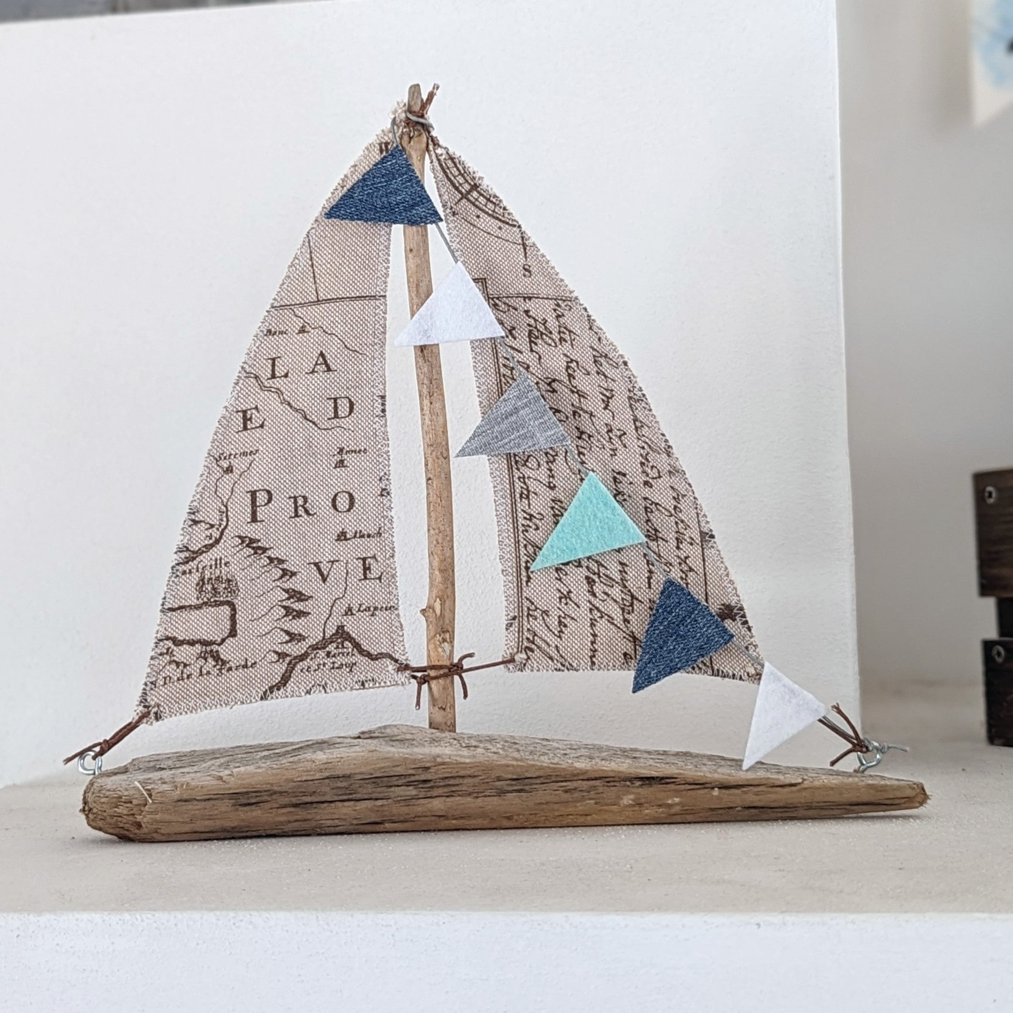Treibholzboot mit Seekarten-Segel und türkis-blauer Wimpelkette