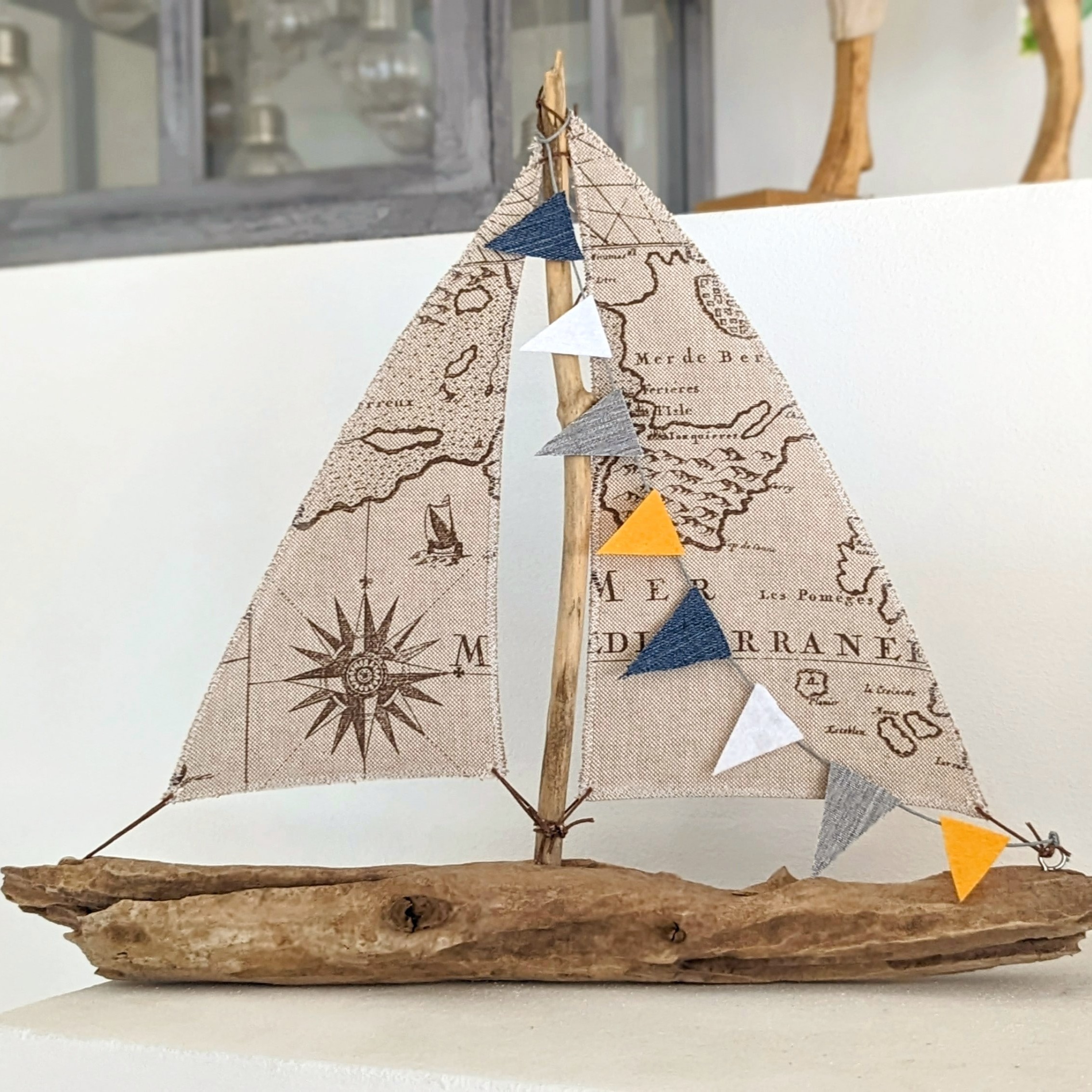 Treibholzboot mit Seekarten-Segel und blau-weiß-oranger Wimpelkette