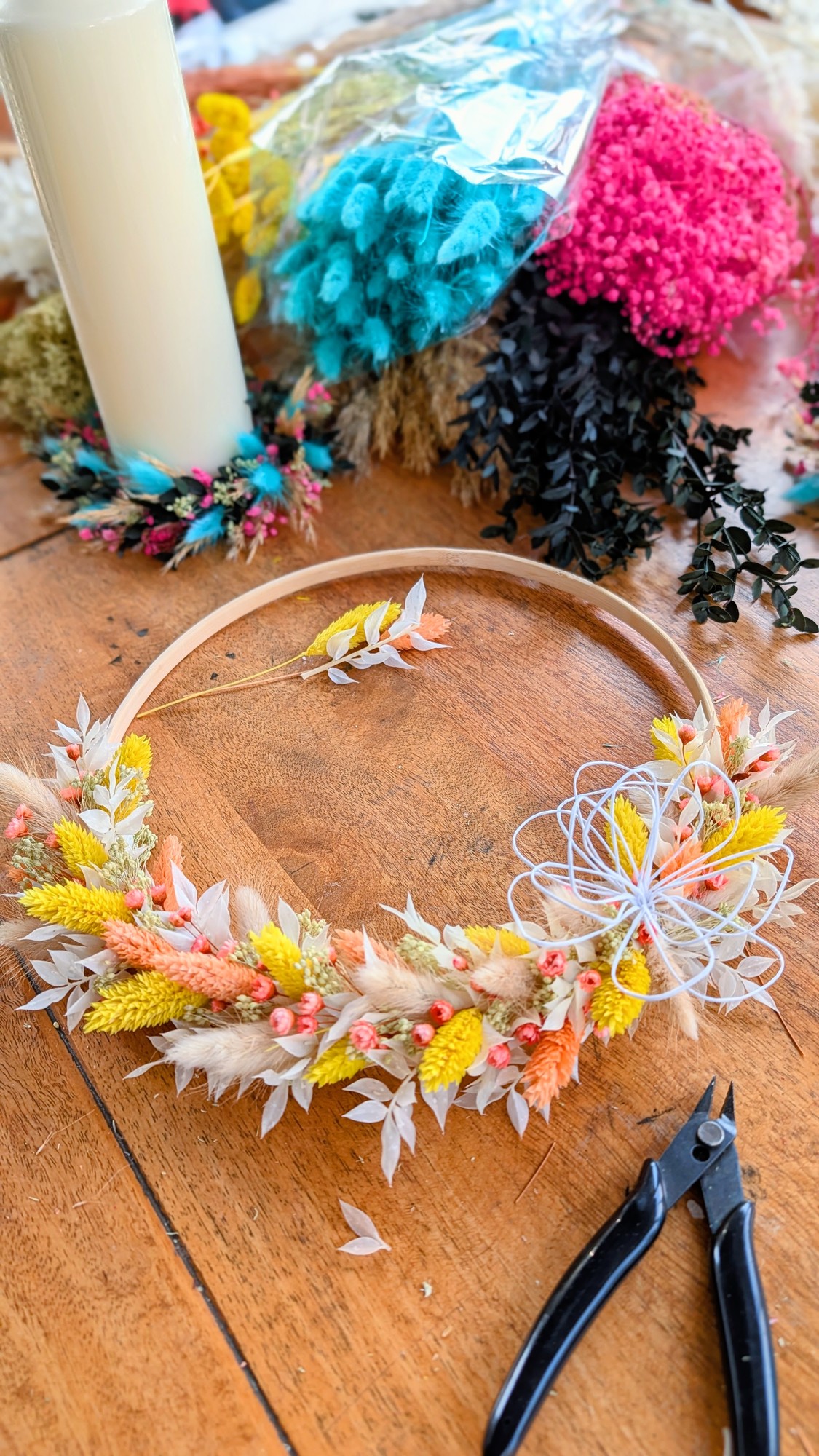 Runder Türkranz aus Holz mit gelb-orangen Trockenblumen und weißer Drahtblüte, in Arbeit auf dem Werktisch